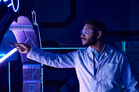 concept futuriste, scientifique indien en lunettes pointant avec stylo au nouvel appareil dans le centre scientifique