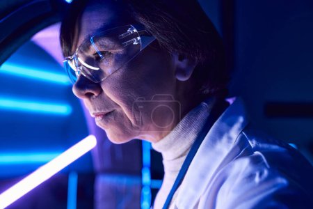 innovative solutions, portrait of middle aged woman scientist in goggles in neon-lit science center