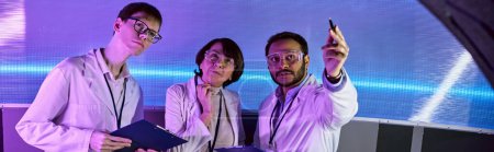 Téléchargez les photos : Homme indien pointant avec stylo près des scientifiques dans le centre de science futuriste néon-éclairé, bannière - en image libre de droit