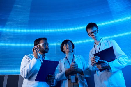 científicos multiétnicos con portapapeles que trabajan en tecnologías futuristas en el centro científico
