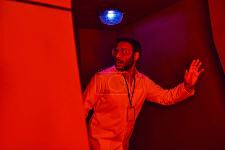 Unbekanntes Phänomen, verängstigter indischer Wissenschaftler schaut in rotem Neonlicht in Innovationszentrum weg