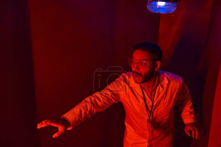 Photo for Shocked indian scientist with outstretched hand in red neon light,  unknown phenomenon - Royalty Free Image