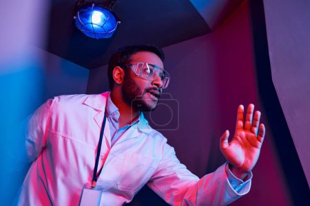 exploration future, scientifique indien inquiet regardant loin sous la lumière du néon dans le centre d'innovation