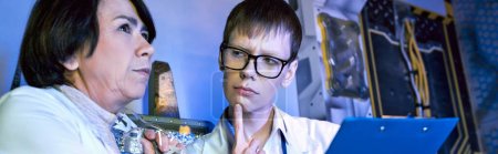 ernsthafte junge Praktikantin blickt auf Wissenschaftlerin mittleren Alters in futuristischem Entdeckungszentrum, Banner