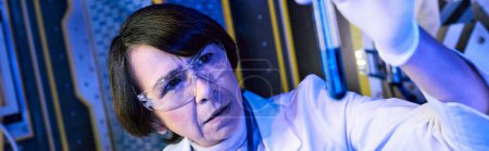 alien life exploration, woman scientist looking at test tube with liquid sample in lab, banner