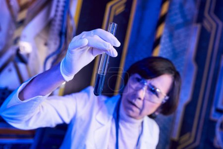 verschwommene Wissenschaftlerin in Latex-Handschuh mit flüssiger Probe im Reagenzglas im Innovationslabor