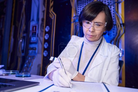Wissenschaft der Zukunft: Wissenschaftlerin schreibt auf Klemmbrett in der Nähe außerirdischer Proben in Petrischalen