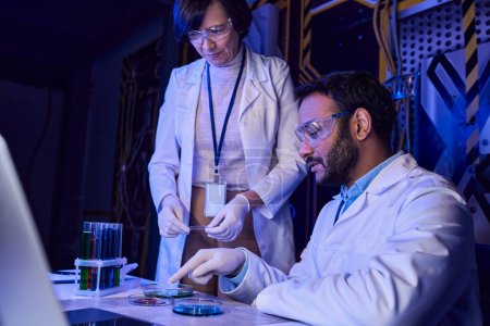indian scientist pointing at petri dishes with samples of otherworldly life near colleague in lab