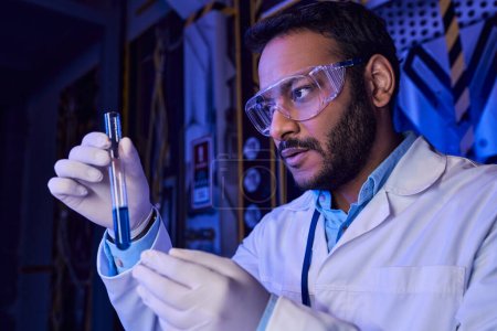 científico indio vanguardista en gafas con muestra líquida en tubo de ensayo, laboratorio futurista