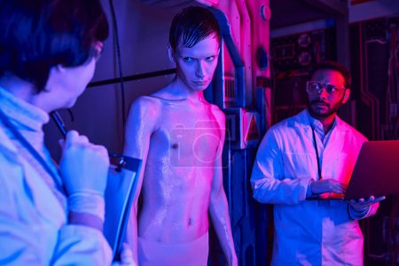 humanoïde alien regardant femme scientifique près de son collègue indien dans un laboratoire innovant