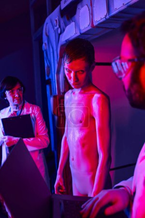 Foto de Científica de mediana edad cerca de alienígena humanoide mirando a su colega en el centro de innovación - Imagen libre de derechos