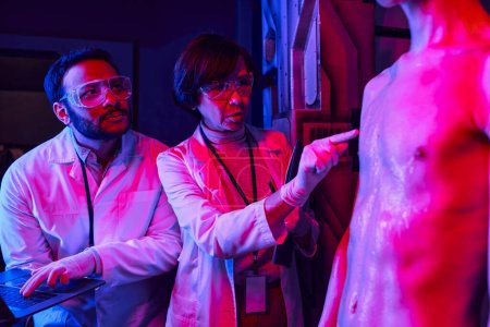 mujer científico tocando extraterrestre criatura cerca india colega con portátil en laboratorio