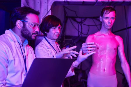 Multiethnische Wissenschaftler mit Laptop untersuchen unbekannten kosmischen Besucher in futuristischem Wissenschaftszentrum