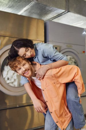 young asian woman piggybacking on smiling boyfriend in blurred public laundry