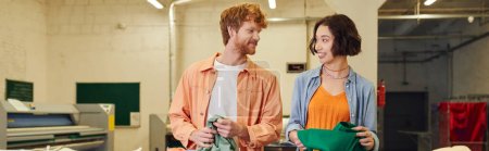 smiling multiethnic couple talking near clothes in public laundry room, banner