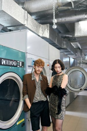 fashionable young multiethnic couple standing near washing machines in public laundry