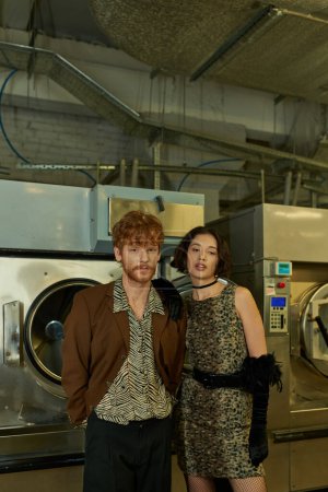 portrait of trendy young multiethnic couple looking at camera in public laundry in evening