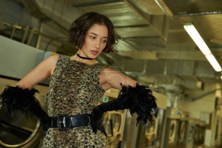 fashionable young asian woman in dress with animal print and gloves posing in coin laundry
