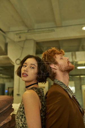 Photo for Stylish young interracial couple standing back to back in public laundry - Royalty Free Image
