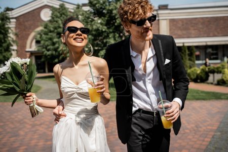 Photo for Interracial couple, sunglasses, wedding attire, orange juice, flowers, happiness, outdoor wedding - Royalty Free Image
