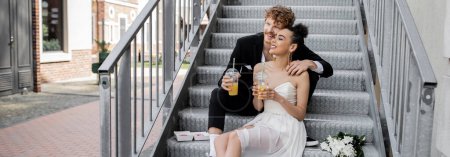 Photo for Wedding on street, pleased interracial couple sitting on stairs with orange juice, banner - Royalty Free Image