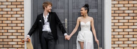Téléchargez les photos : Interracial jeunes mariés avec longboard et skateboard, bâtiment, regarder les uns les autres, bannière - en image libre de droit