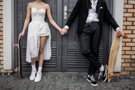 Téléchargez les photos : Couple interracial en tenue de mariage, avec longboard et skateboard près du bâtiment de la ville, vue dégagée - en image libre de droit