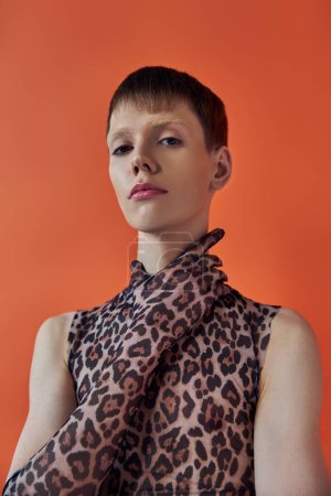 queer fashion concept, young man posing on orange backdrop, sleeveless animal print, leopard print