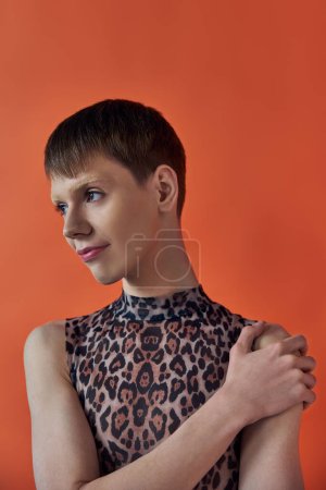 queere Mode, fröhliche nichtbinäre Person, die lächelt und wegsieht, orangefarbener Hintergrund, Animal Print