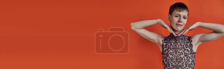 androgynous person smiling and posing on orange backdrop, hands near face, queer fashion, banner