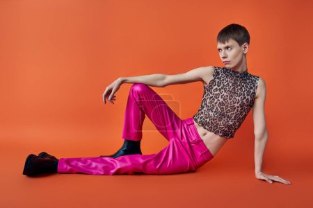 nichtbinäre Person in Leopardenmuster ärmelloses Oberteil und rosa Hose auf orangefarbenem Hintergrund, queere Mode