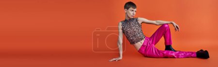 nonbinary person in leopard print top and pink pants on orange backdrop, queer fashion, banner