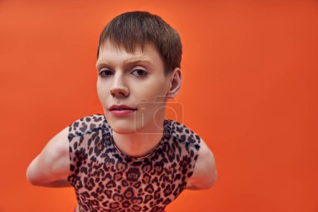 modelo queer en estampado de leopardo sin mangas superior mirando a la cámara, fondo naranja, tendencia de moda