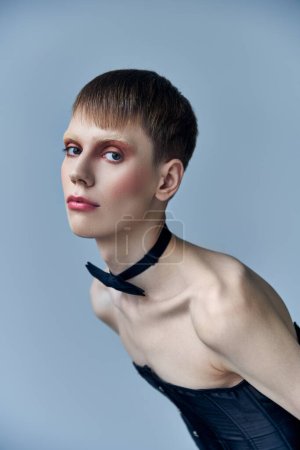 Queer Model mit Make-up vor der Kamera, grauer Hintergrund, Mode und Trend, Fliege, androgyn