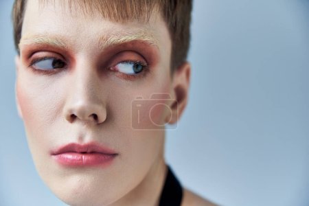 Nahaufnahme, androgyne Person mit Make-up, grauem Hintergrund, Schönheit und Visage, queer, Porträt