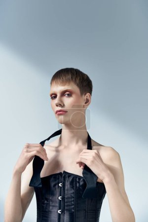 queer person with corset touching tie and posing on grey backdrop, beauty, makeup, androgynous