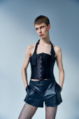 queer model in black corset and shorts posing with hands in pockets on grey backdrop, androgynous puzzle #669096200