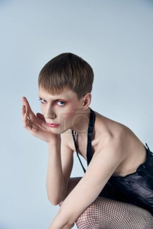 Modell in schwarzem Korsett und Netzstrumpfhose vor grauem Hintergrund, androgyne Person, queere Mode