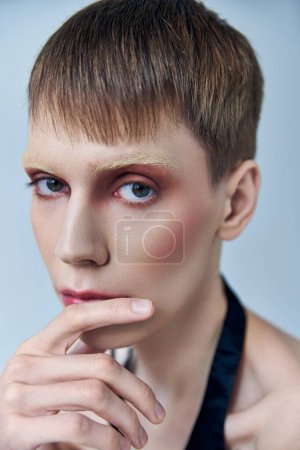 queere Person mit Make-up, die vor grauem Hintergrund wegschaut, androgyne Person, Porträt, Identität
