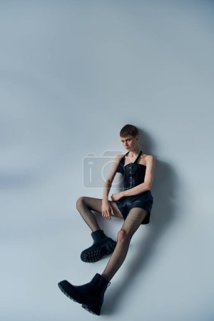 Androgynes Model in Korsett, Shorts und Netzstrumpfhosen posiert vor grauem Hintergrund, lgbt, queer fashion
