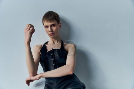 androgynes Modell in schwarzem Korsett posiert vor grauem Hintergrund, queer fashion, lgbtq, edgy style