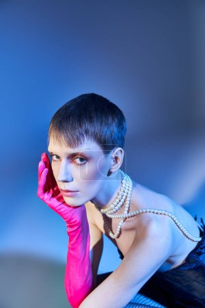 Photo for Nonbinary person in corset and pink glove posing on blue backdrop, queer model, self expression - Royalty Free Image