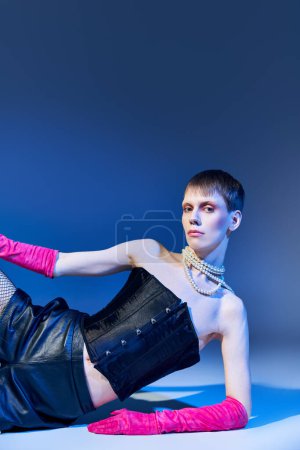 queer model in bold outfit and pink gloves posing on blue backdrop, shorts, nonbinary, style