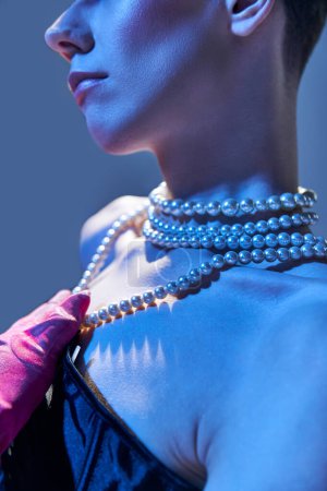 close up and details, genderfluid model with pearl necklace posing in pink glove on blue backdrop