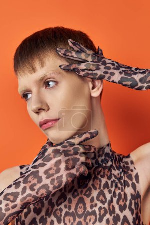Nahaufnahme eines queeren Models im Animal-Print-Outfit, das auf orangefarbenem Hintergrund posiert, stylisches Genderfluid