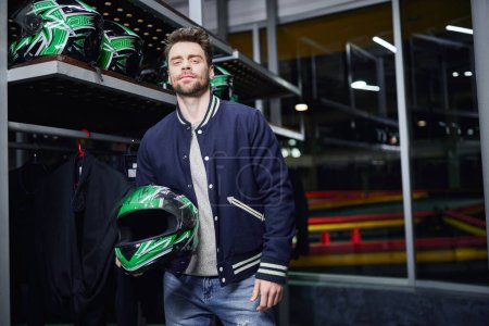 Sportlicher Kart-Rennfahrer mit Helm in der Hand und Blick in die Kamera, männlicher Fahrer, Go-Kart-Konzept