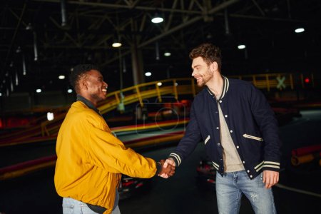 hombre afroamericano feliz estrechando la mano con amigo dentro de pista de karting, competencia