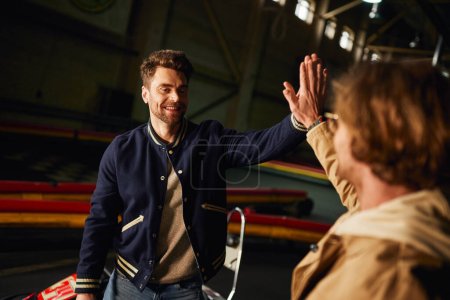 Photo for Excited male friends giving high five to each other inside of karting racing track, teamwork and win - Royalty Free Image