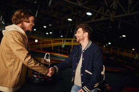 hombre feliz en gafas estrechando la mano con un amigo dentro de la pista de karting, competencia