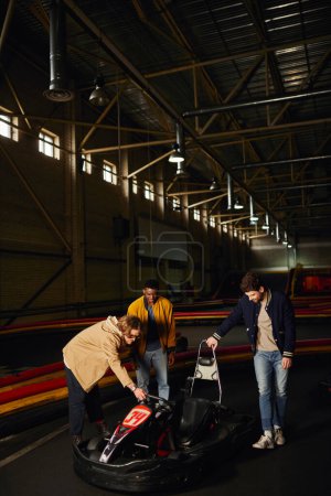 Fröhliche Mischlingsfreunde stehen neben rotem Go-Kart auf Indoor-Bahn, Motorsport-Hobby